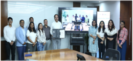 Battery and energy storage researchers standing together in a row in a room with a large screen in the center showing people.