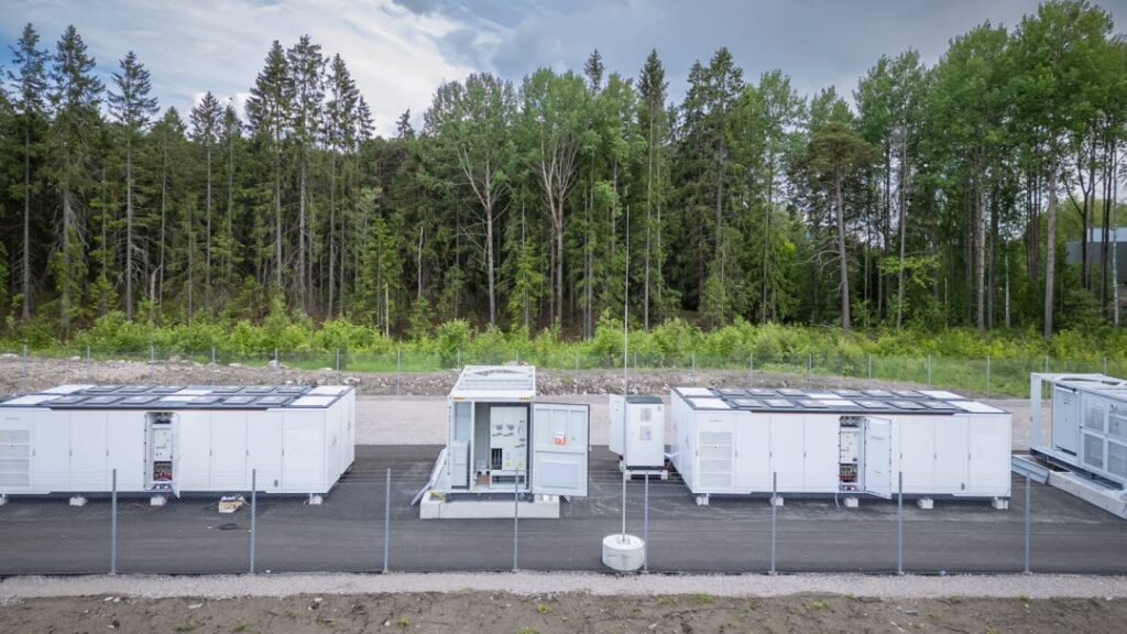 Battery energy storage systems developed by Ingrid Capacity at a site in Sweden surrounded by green trees.